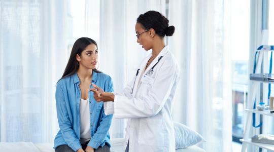Young Black woman doctor speaks with young Latina patient
